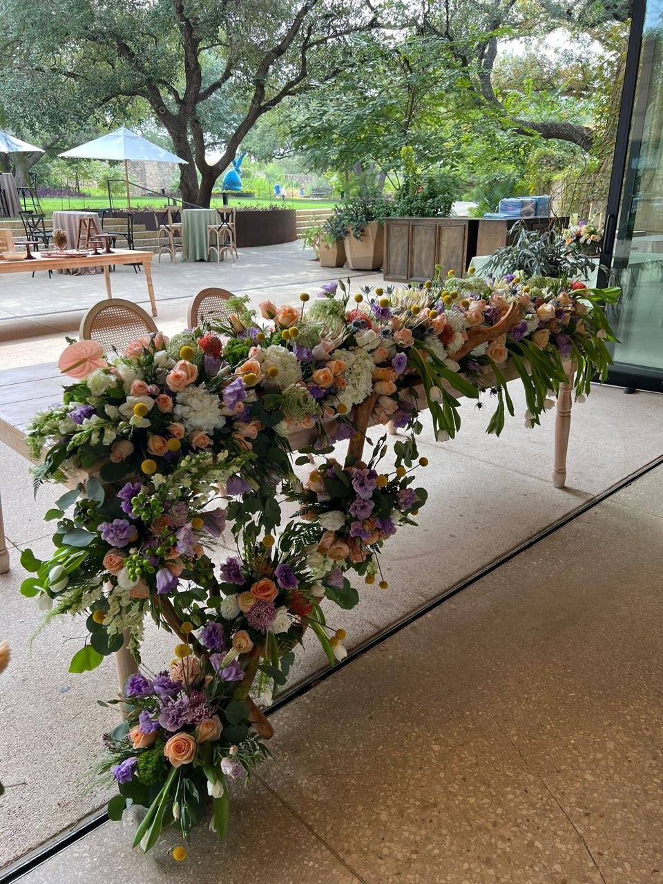 Cascading floral runner in peach, plum and cream blooms spilling over the edge of a table against a wall of greenery