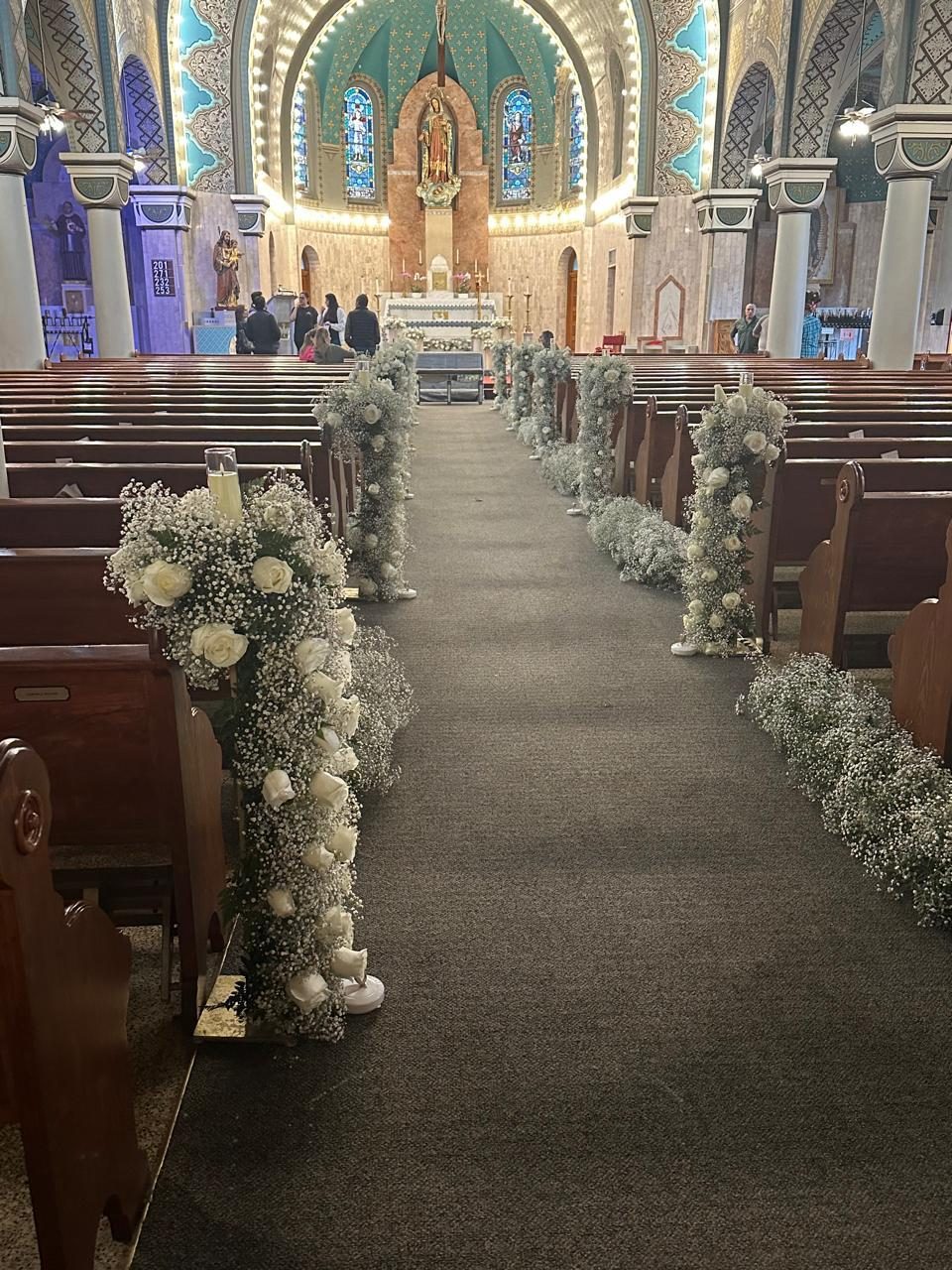 Church aisle lined with white floral and baby&rsquo;s-breath arrangements leading to the altar