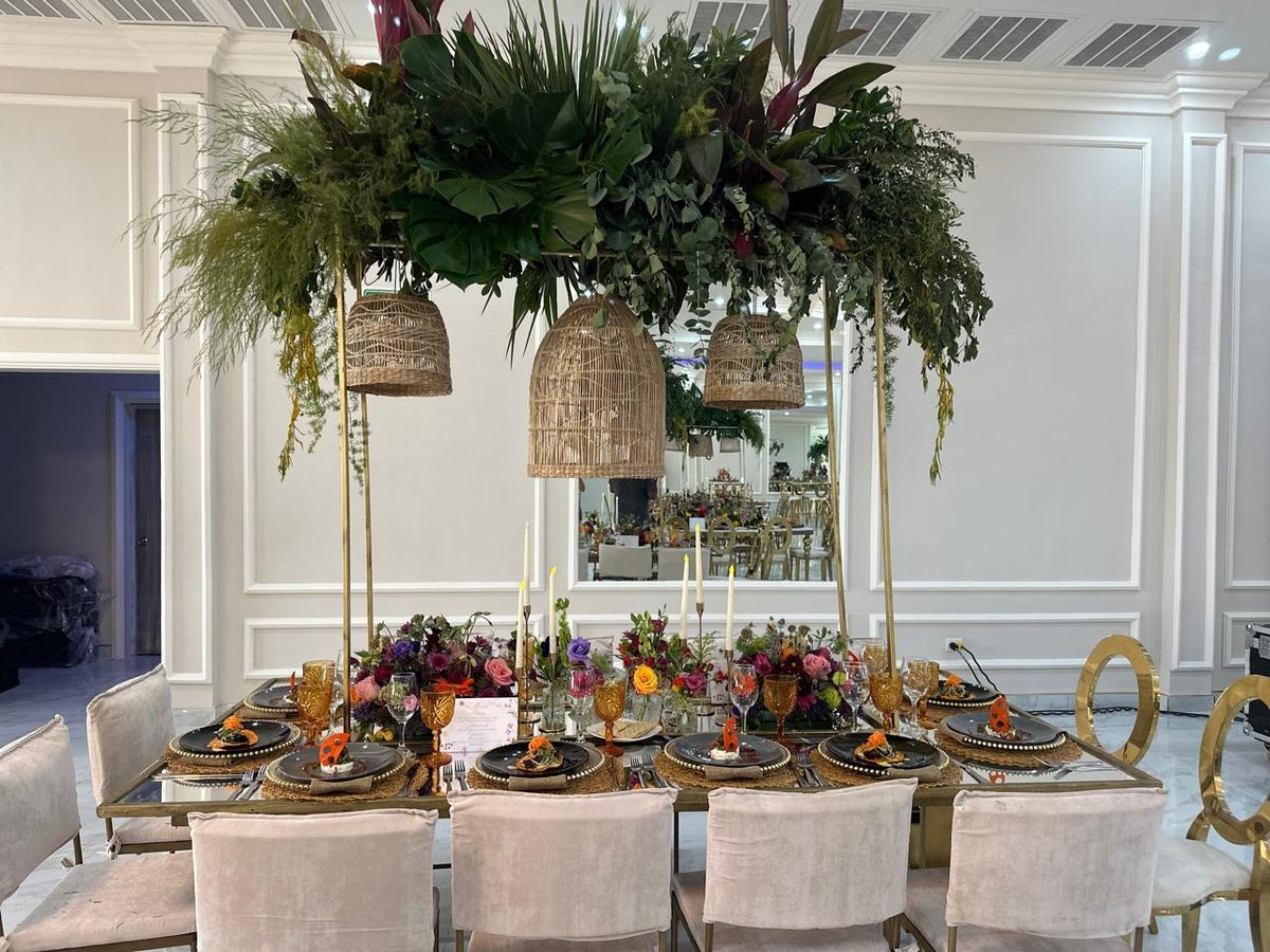 Elevated tropical greenery arrangement with woven pendant lanterns above a set dinner table