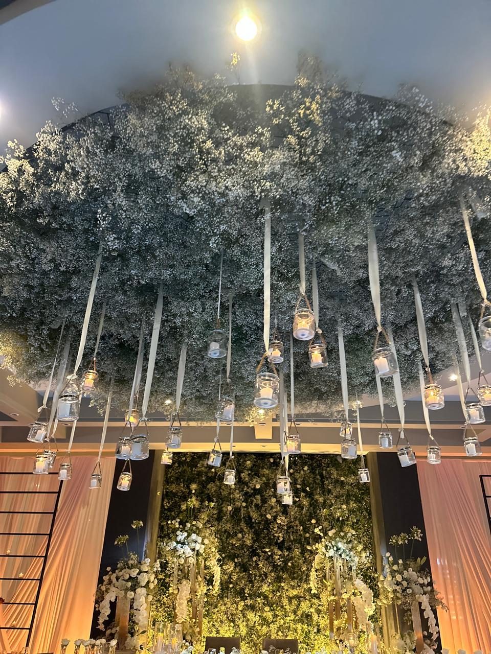 Dense baby&rsquo;s-breath canopy with hanging glass candle vessels above a long head table