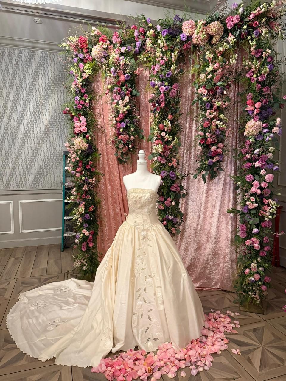Floral archway in pink and burgundy blooms with draped fabric framing a displayed gown