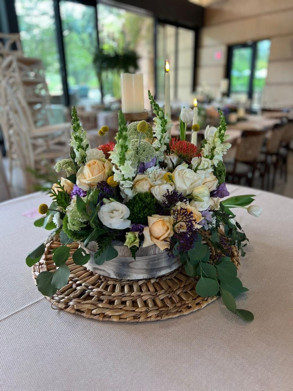 Garden-style floral centerpiece in cream, burgundy and plum on a woven rattan base