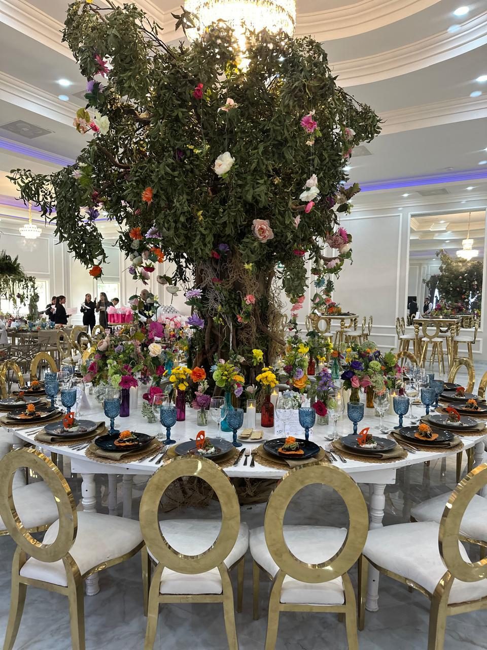 Full flowering tree installed as a centerpiece rising above a long reception table with colourful bud vases