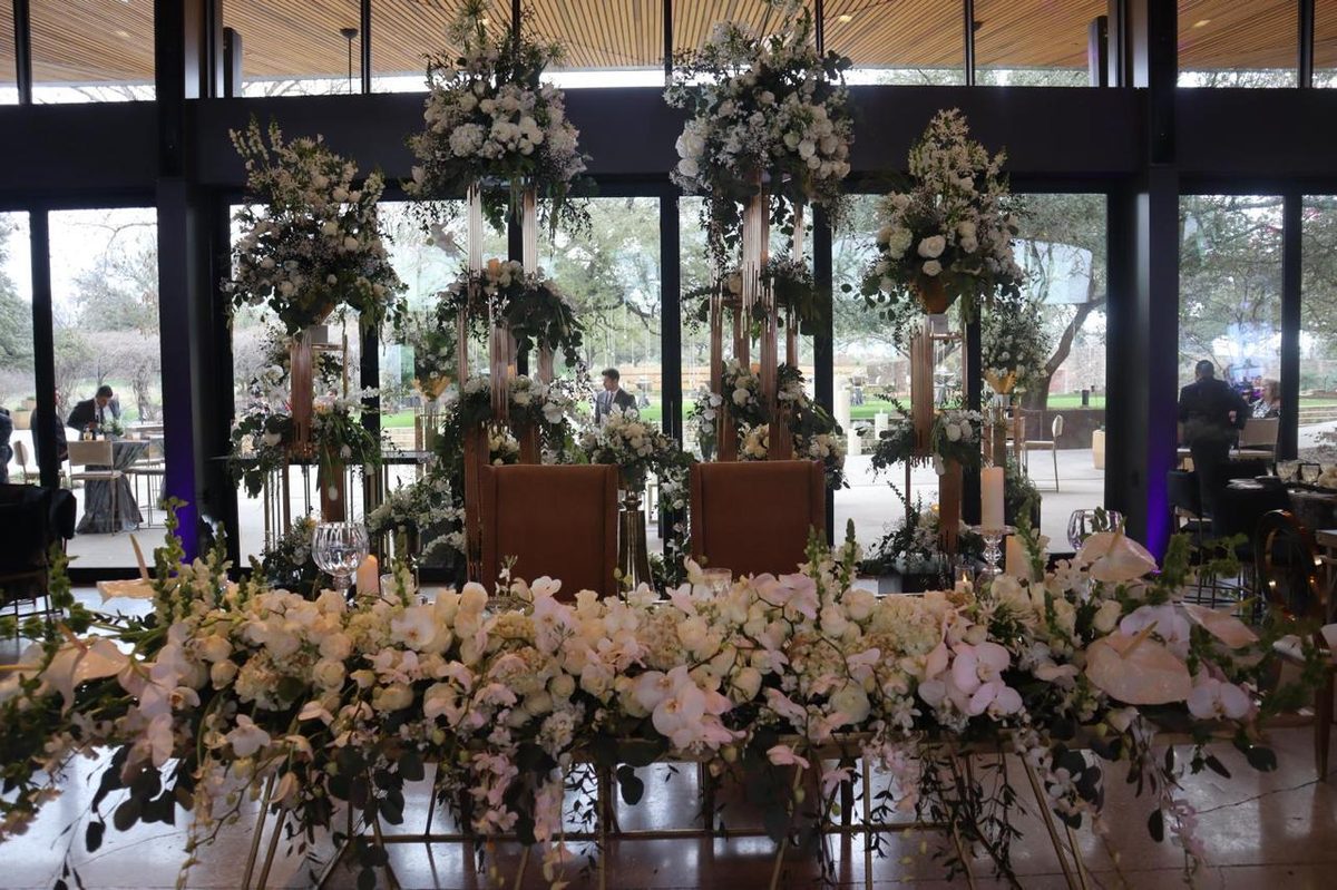 Long head table massed with dried and blush florals set against a wall of windows