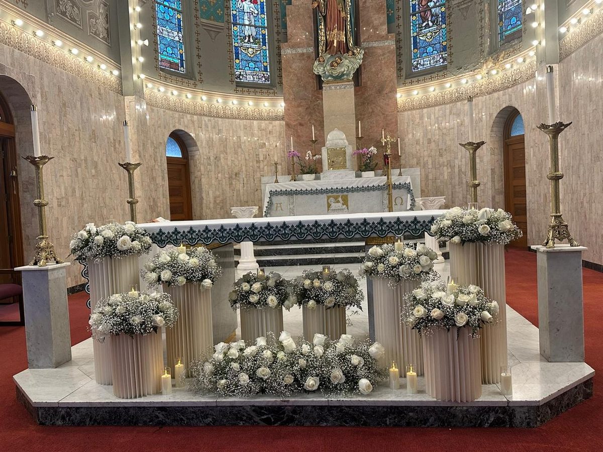 Church altar dressed with white roses, hydrangea and baby&rsquo;s breath beneath stained glass