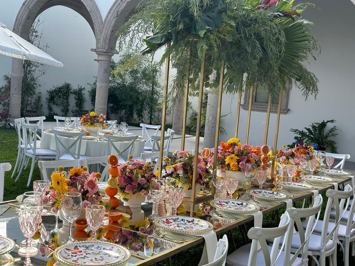 Garden reception with tall palm and fern centerpieces above a brightly coloured tablescape