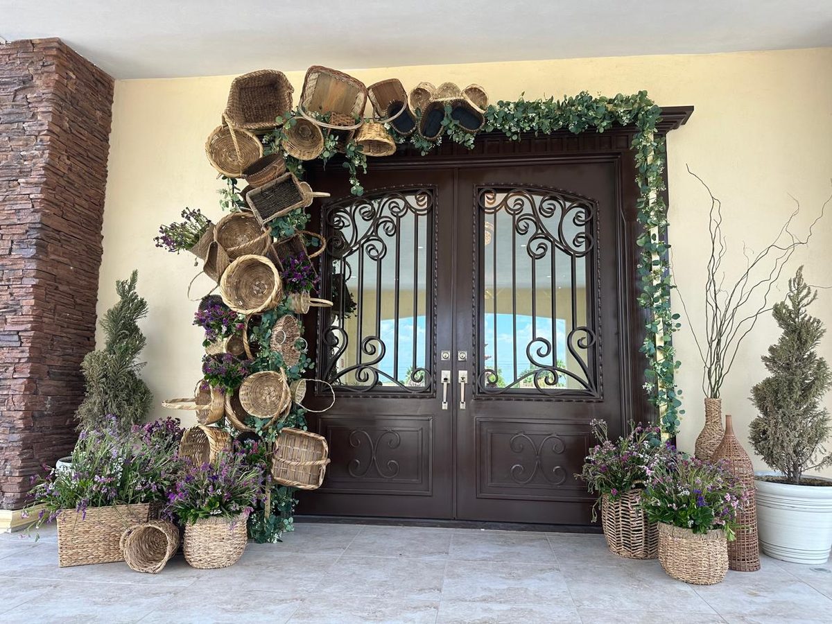 Timber double doors framed by an arch of woven baskets, greenery and dried florals