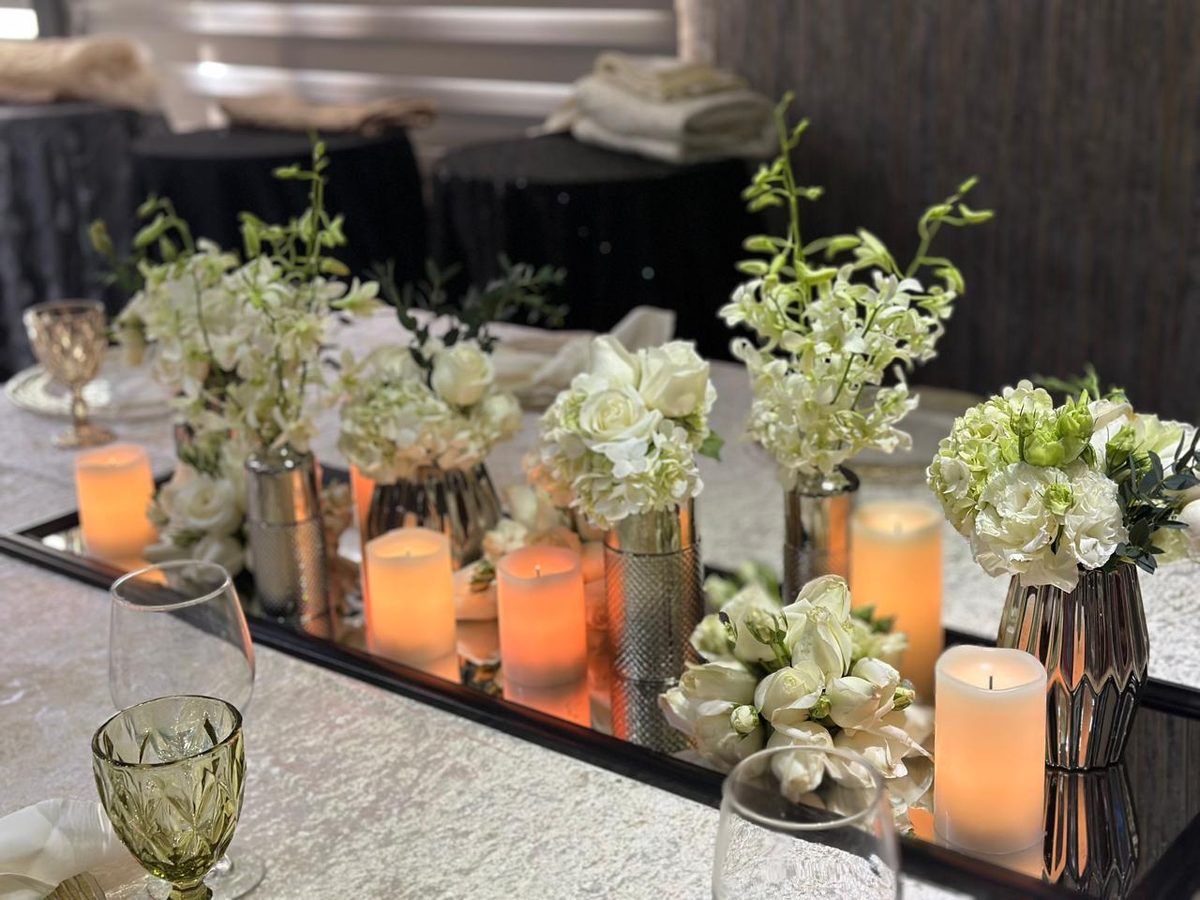 Low runner of white roses, orchids and hydrangea threaded with pillar candles in glass
